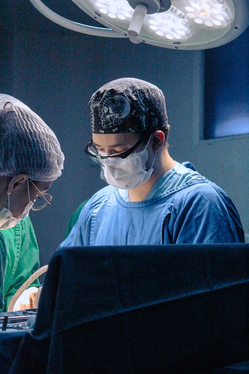 Dr. Richard Brasil em centro cirúrgico, de touca, máscara e óculos de proteção, durante uma cirurgia